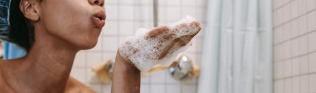 Kvinne med skum i hånden i dusjen, vegansk og sulfatfri hårpleie