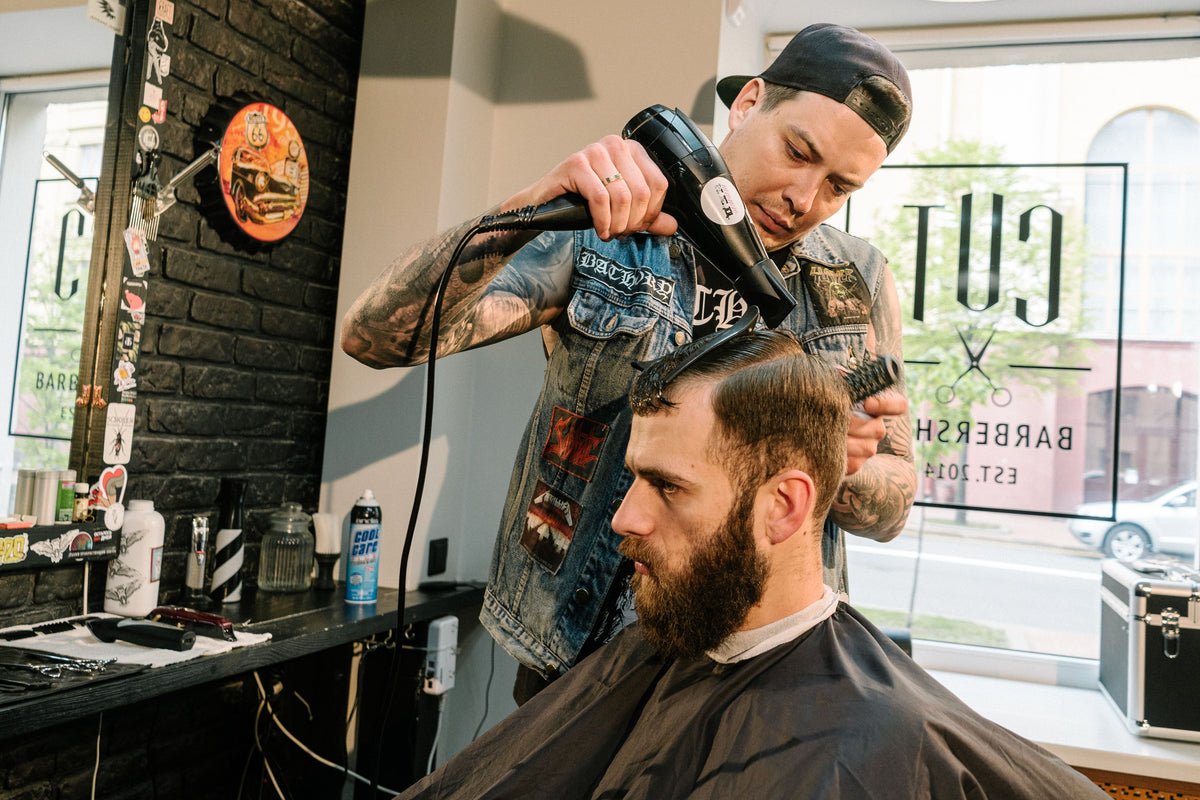 Frisør føner håret til en kunde i barbersalong – volumtriks før styling