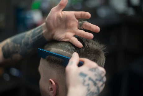 Friseør med tatoveringer stiler hår med blå kam i barberbutikk