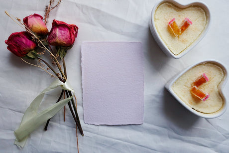 Tørre roser, lilla papir og hjerteformet kake på hvit stoffbakgrunn